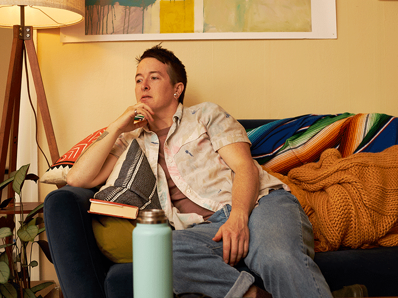 non binary person sitting on couch looking away