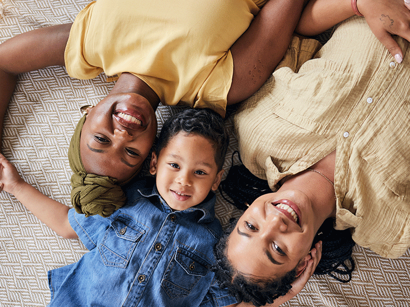 LGBT, happy portrait and relax family, child or people care, smile and lesbian bond together, lying and on floor carpet. Mothers face, top view kid and non binary parents, homosexual mom or gay women