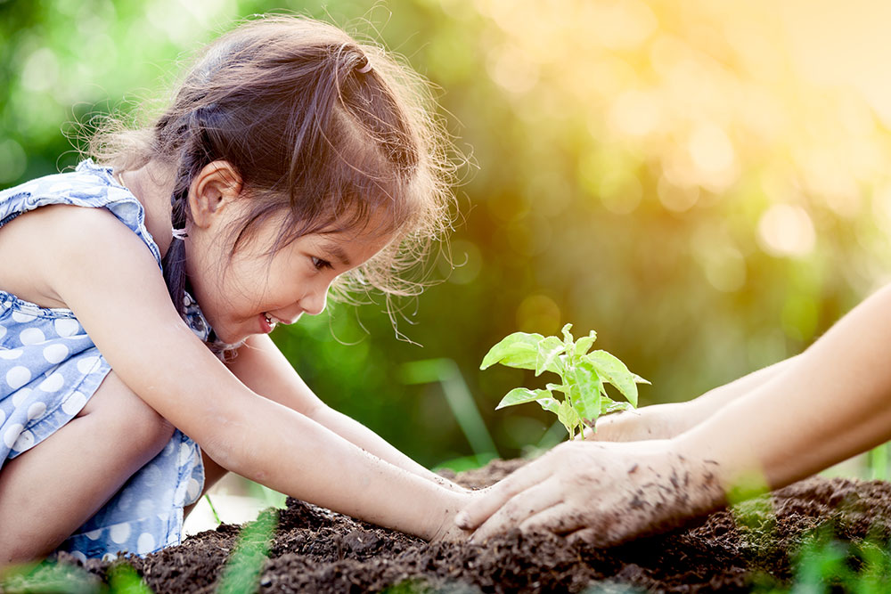Asian little girl and parent planting young tree on black soil together as save world concept in vintage color