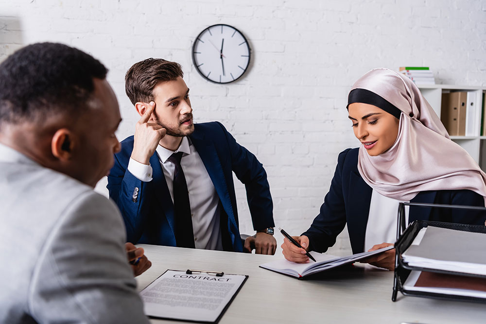 arabian businesswoman writing in notebook during negotiation with interracial business partners, blurred foreground