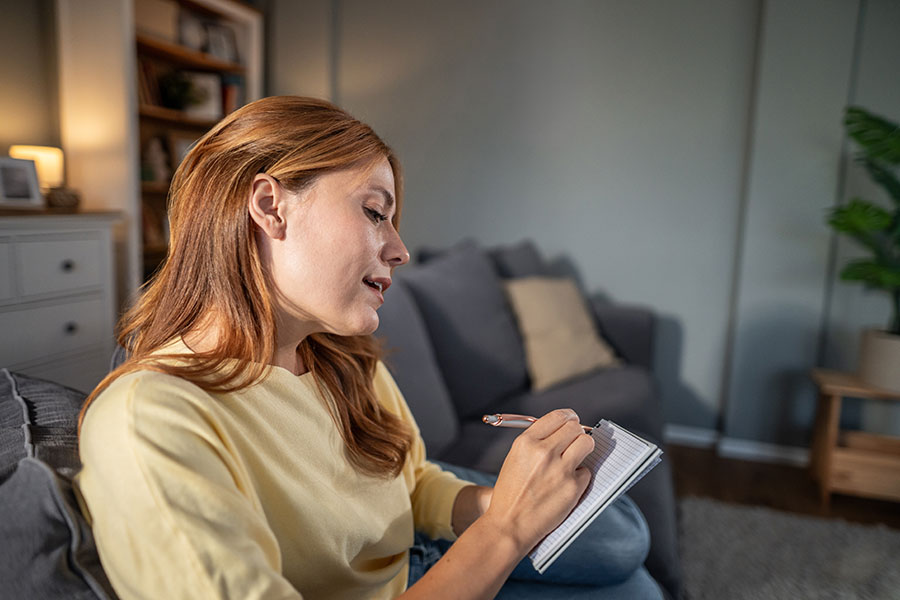 Woman writing notes in notebook at home