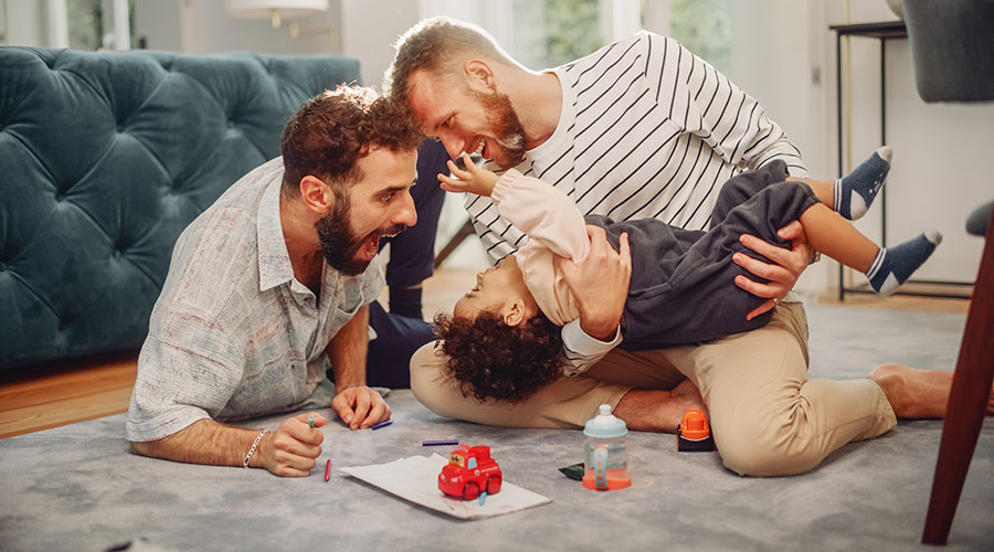 Loving LGBTQ Family Playing with Toys with Adorable Baby Boy at Home on Living Room Floor